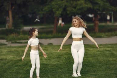 Mother and daughter bonding through outdoor exercise in activewear, featuring a joyful moment in a green park.